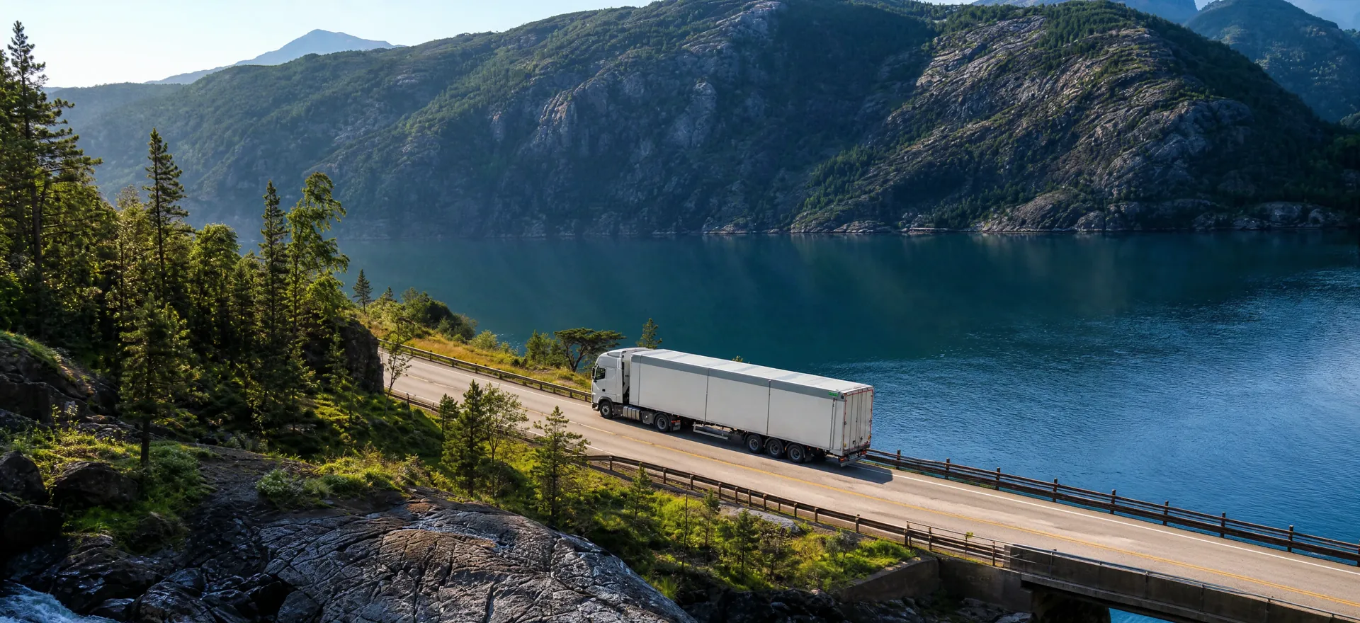 A white truck driving along a mountain road beside a fjord